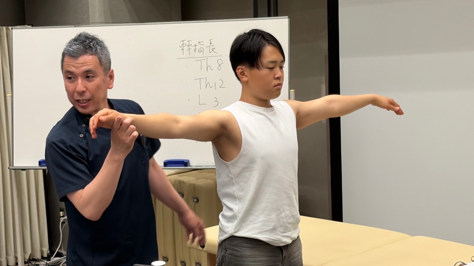 受講生の腕を支えながら、肩関節の動きを解説する院長